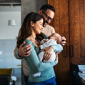 A smiling couple, embracing and looking adoringly at the newborn baby in the woman's arms